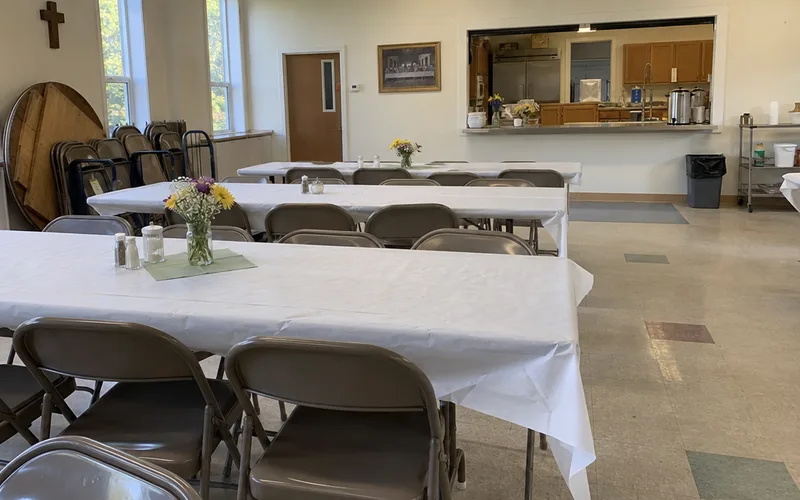 Church fellowship hall with long folding tables and a kitchen serving window