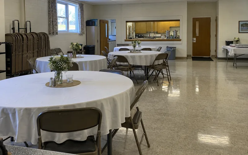 Community hall with round tables, white tablecloths and stacked chairs before a wedding