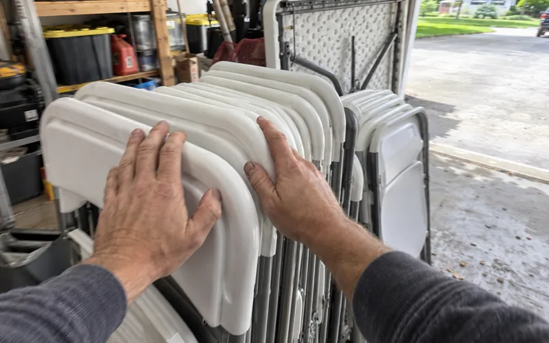 Hands resting on a stack of rented folding chairs in a garage