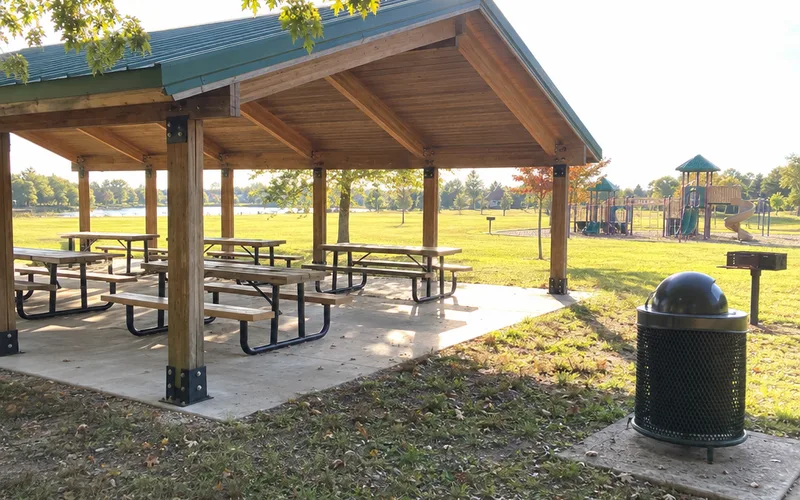 Open-sided park pavilion with picnic tables under a green metal roof