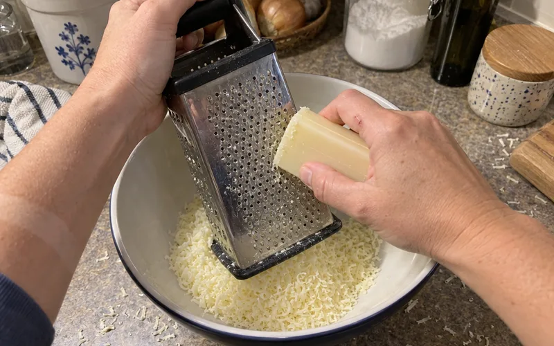Hands grating a bar of laundry soap into fine shreds over a mixing bowl