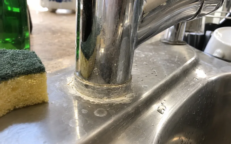 White chalky hard water crust around the base of a kitchen faucet