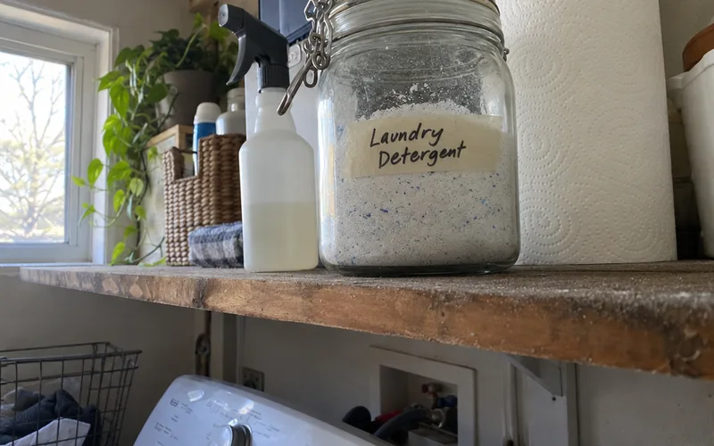 Sealed jar of homemade laundry detergent with a tape label on a high laundry room shelf