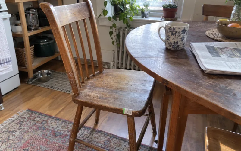 Secondhand wooden chair with a thrift store sticker at a dining table