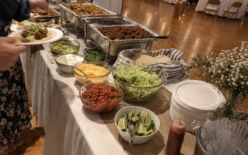 Self-serve taco bar with trays of fillings and paper plates at a casual wedding reception